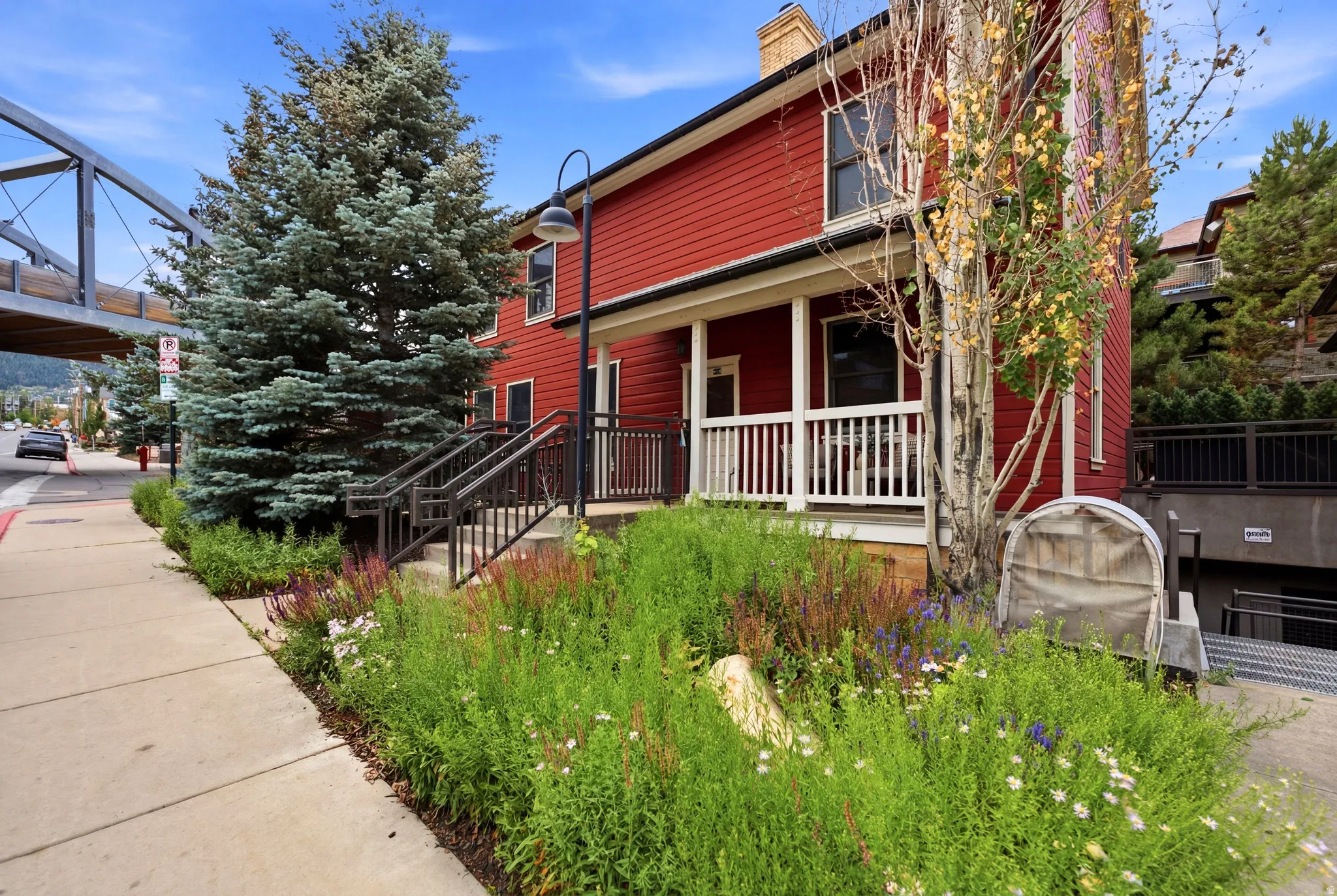 Red siding exterior with white trim, covered front porch, wrought iron railing, mature evergreen trees, and established ground cover landscaping