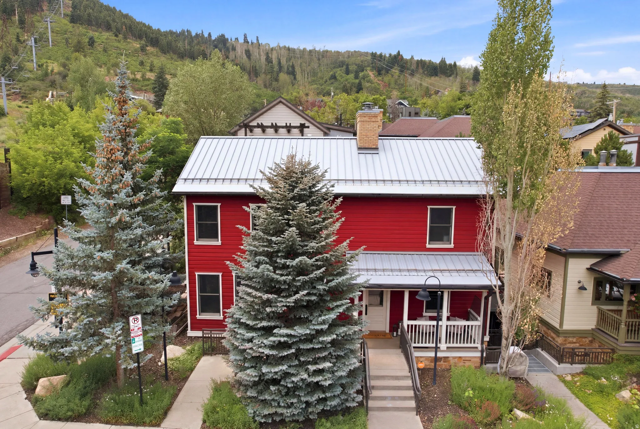 Red exterior with a corrugated metal roof, front porch with white railings, and mature trees
