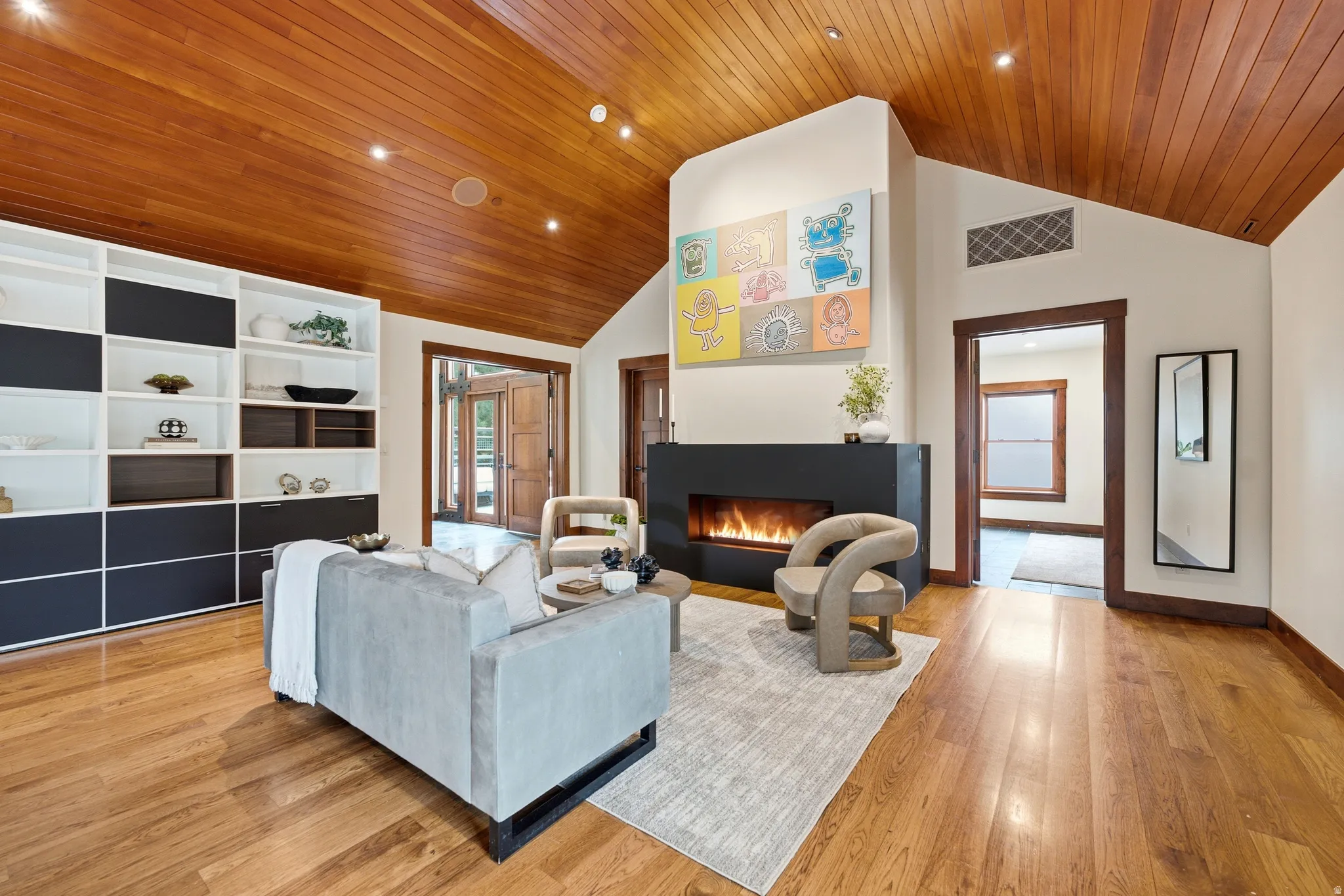 Vaulted wood-finish ceiling, hardwood flooring, built-in shelving, linear fireplace, and wood-frame double doors