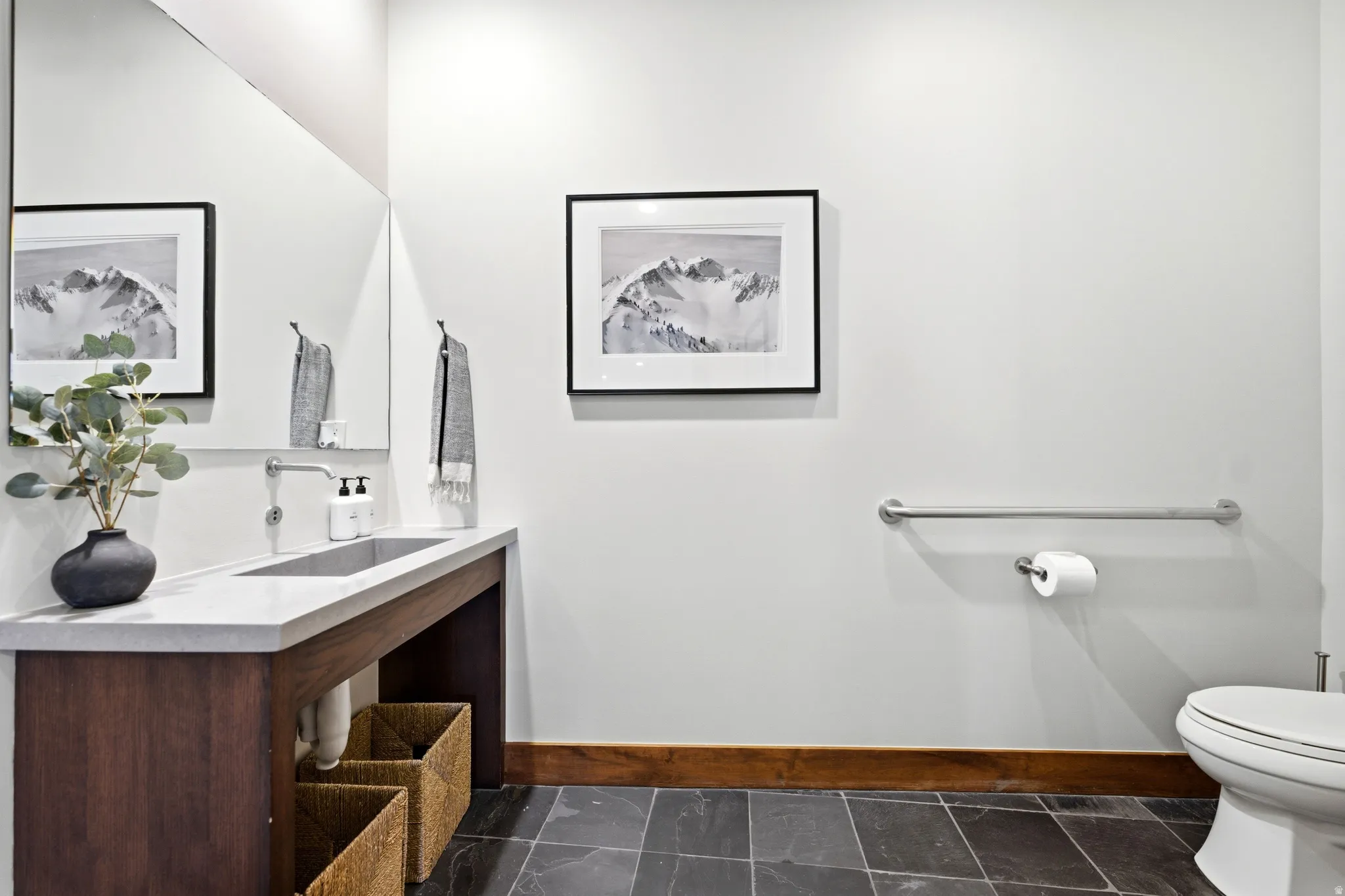 Integrated rectangular basin with a wall-mounted faucet, wood vanity, large wall mirror, and dark tile flooring