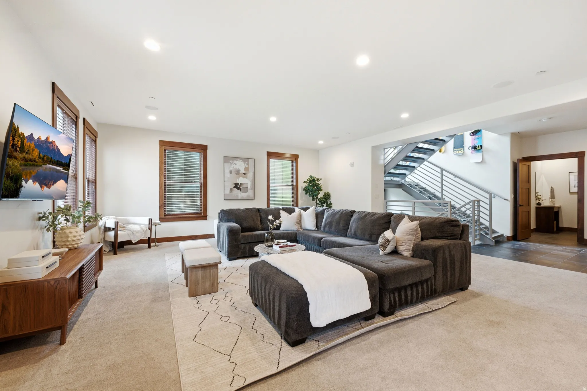 Spacious living area featuring recessed lighting, multiple windows with wood trim, and a prominent open staircase with metal railings