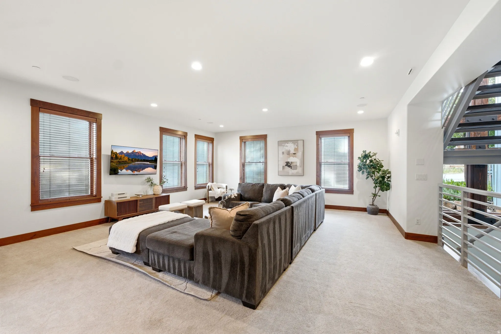 Recessed lighting, wood-trimmed windows, light-toned carpeting, and a contemporary metal staircase with railing