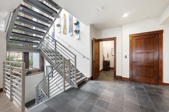 Open-riser metal staircase with horizontal railings, dark wood-finish doors, dark wood window trim, and dark tile flooring