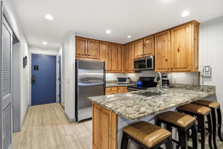 Wood-finish flooring leading to a kitchen with granite countertops, stainless steel appliances, wood cabinetry, and recessed lighting