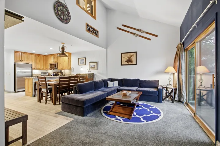 Vaulted ceilings with track lighting, open-concept layout, wood-finish flooring, full kitchen with stainless steel appliances, and sliding glass door