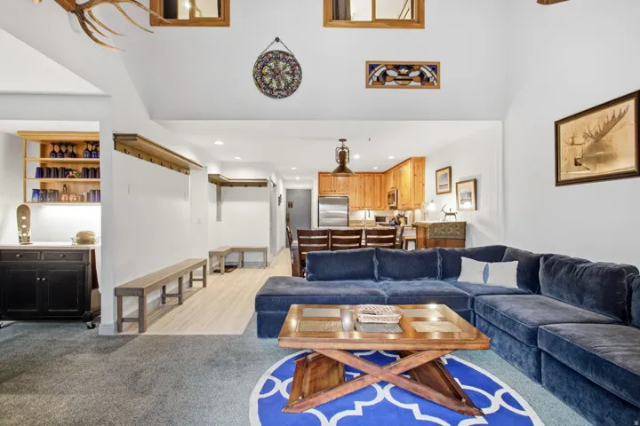 Vaulted ceilings with recessed lighting, wood-finish flooring, a built-in wet bar with cabinetry, and a kitchen featuring wood cabinetry and stainless steel appliances
