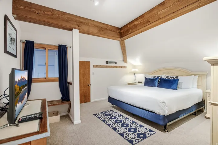 Vaulted ceilings with exposed wood beams, neutral-toned carpeting, wood-finish window frames, and wood-finish door