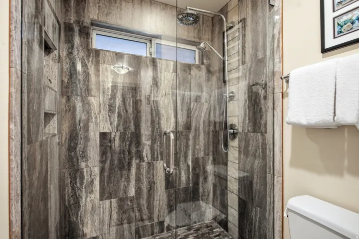 Walk-in shower with full-height stone-look tile, glass enclosure, recessed niches, built-in bench, and rain showerhead