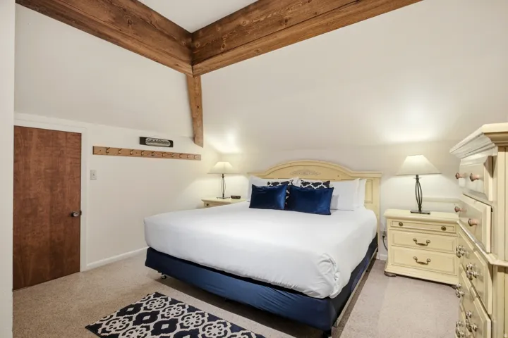 Exposed wood beam ceiling, wood-finish door, wall-mounted wooden rack, recessed lighting, and carpeted flooring