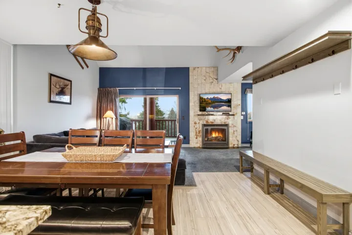 Wood-finish flooring, built-in fireplace with stone-finish surround, wood dining table with seating, sliding glass door, and a built-in bench with coat hooks