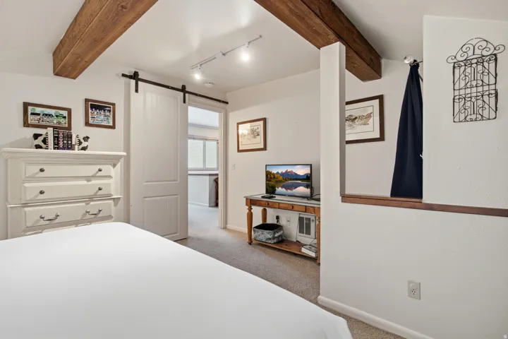 Exposed wood ceiling beams, track lighting, barn-style sliding door, and a built-in wood-finish half-wall