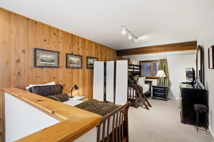 Vertical wood-paneled accent wall, exposed wood beam ceiling, track lighting, and carpeted flooring