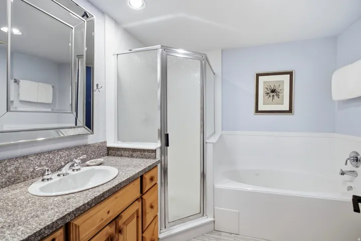 Built-in corner shower with a frameless glass enclosure, a white soaking tub, wood-finish vanity with a drop-in sink, and a framed mirror