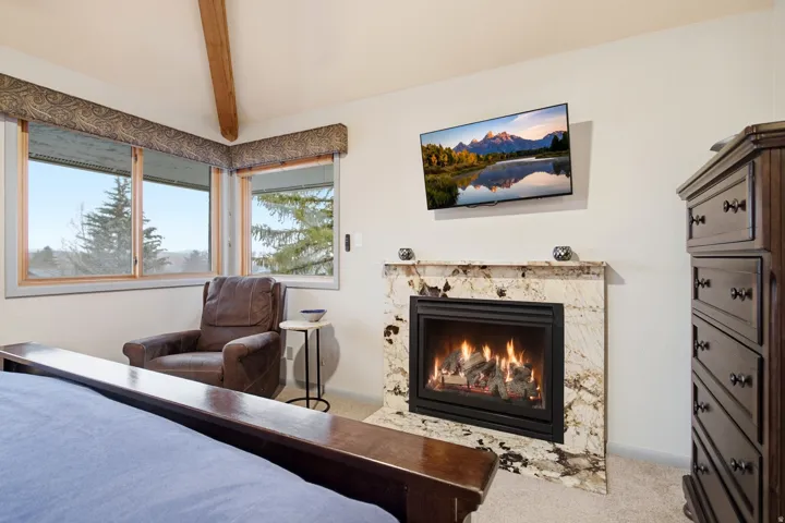 Fireplace with a stone surround, wall-mounted television, and wood-framed windows