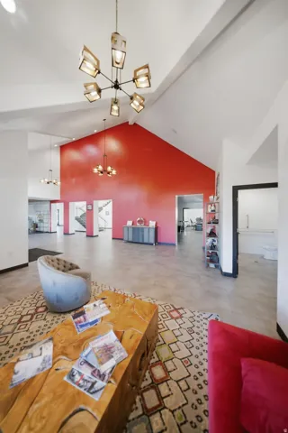 Vaulted ceilings with exposed beams, multiple contemporary chandeliers, a vibrant accent wall, and tiled flooring
