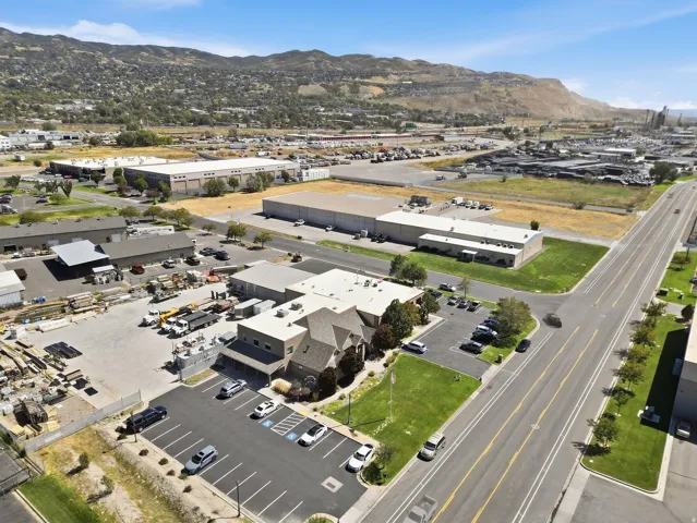 Commercial property featuring a multi-level building with an asphalt parking lot, paved access roads, and surrounding industrial structures