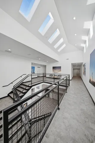 Vaulted ceiling with multiple skylights, extensive black metal railing, concrete-finish flooring, and recessed lighting