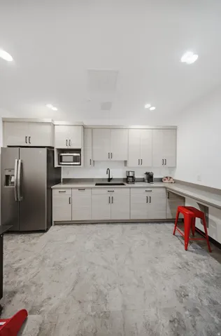 Stainless steel refrigerator, built-in microwave, dark countertop with undermount sink, light wood-finish cabinetry, and recessed lighting