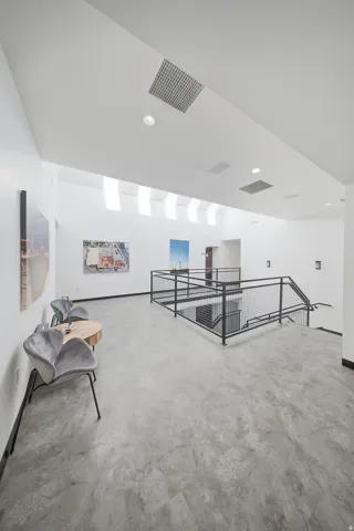 Concrete-finish flooring, white walls, black metal railing, recessed ceiling lighting, and skylights