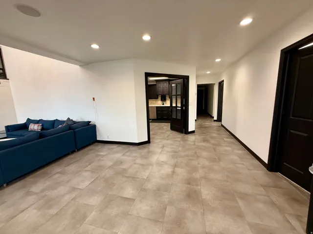 Spacious interior featuring large format floor tiling, recessed lighting, solid panel doors, and a partial glass-paneled door