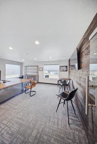 Recessed ceiling lighting illuminates the space featuring a wood-finish accent wall, multiple windows, and patterned carpeting