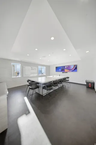 Recessed lighting, white ceiling, white walls, dark flooring, and a long white table