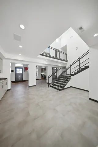 Spacious interior with light-toned tile flooring, contemporary metal stair railing, recessed ceiling lighting, and a second-story balcony