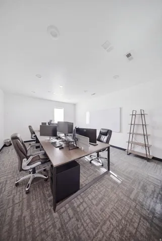 Recessed lighting, white walls, gray patterned carpeting, and a built-in whiteboard