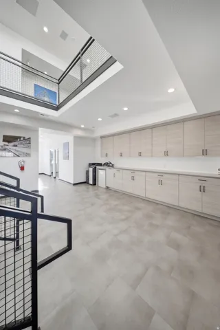 Open-concept space featuring a second-story balcony with metal railing, recessed lighting, wood-finish cabinetry, light-toned countertops, and large format tile flooring