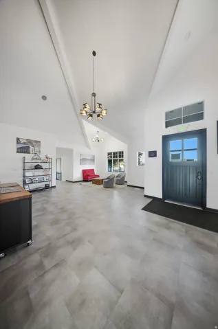 Vaulted white ceilings with exposed beams, plank-style flooring, a dark paneled entry door with transom window, and a modern chandelier