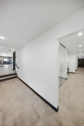 Spacious hallway with light-toned tile flooring, recessed lighting, and modern glass-paneled rooms