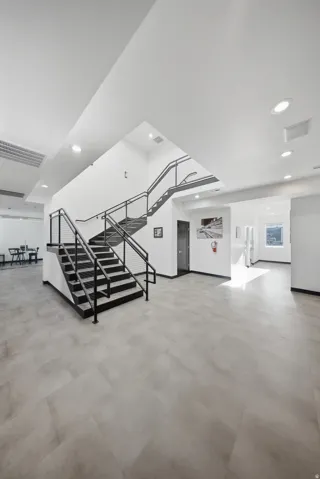 Spacious interior featuring a contemporary black metal staircase with cable railings, recessed lighting, and large format tile flooring