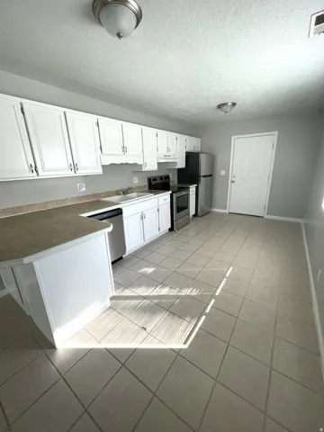 Kitchen featuring white cabinetry, light-toned countertops, a stainless steel refrigerator, a built-in dishwasher, and neutral tile flooring