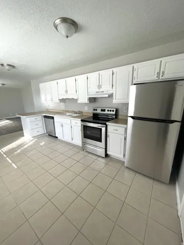 Kitchen featuring white cabinetry, stainless steel appliances, neutral countertops, and tile flooring