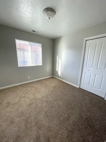 Carpeted room featuring a double-pane window with blinds, a flush mount ceiling light fixture, and bifold closet doors