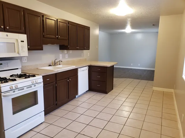 Kitchen featuring dark wood-finish cabinetry, white appliances, and light-toned countertops