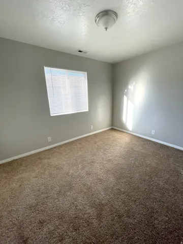 Neutral-toned walls, brown carpeting, and window with horizontal blinds