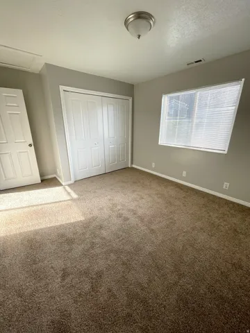 Carpeted room with a ceiling-mounted light fixture, louvered window blinds, and bi-fold closet doors