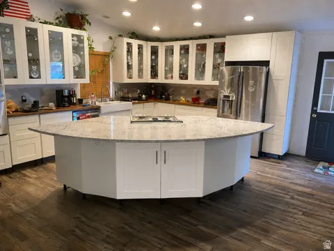 Spacious kitchen featuring an expansive center island with cooktop, white cabinetry with glass-front upper doors, wood-finish flooring, and recessed ceiling lighting