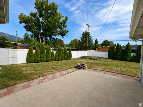 Expansive backyard with a concrete patio featuring a brick paver border, mature privacy plantings, and a white vinyl fence