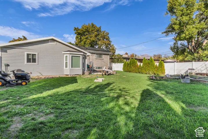 Expansive backyard with a manicured lawn, a white privacy fence, and mature trees