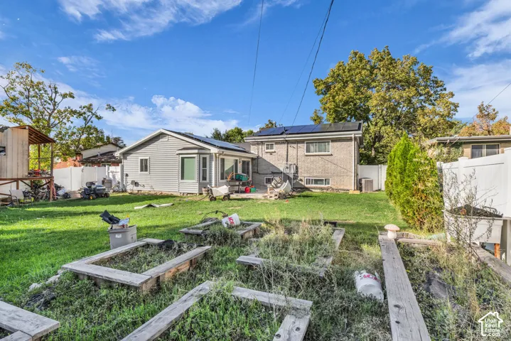 Expansive backyard featuring a green lawn, wood-framed garden beds, and a white privacy fence
