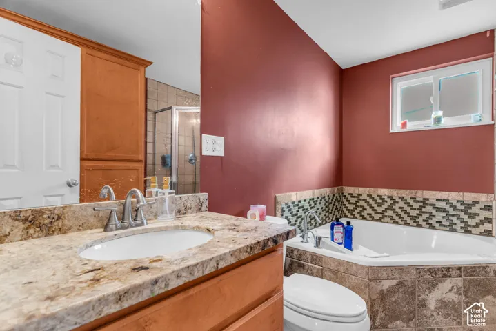 Bathroom featuring a built-in corner soaking tub, vanity with a stone countertop and undermount sink, and a tiled shower enclosure