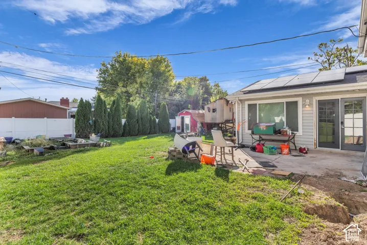 Expansive grass backyard with a concrete patio, white privacy fencing, and mature trees