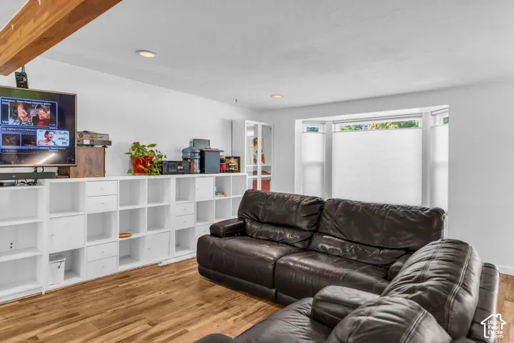 Living space featuring wood-finish flooring, recessed lighting, a prominent wood beam, white built-in shelving, and a bay window