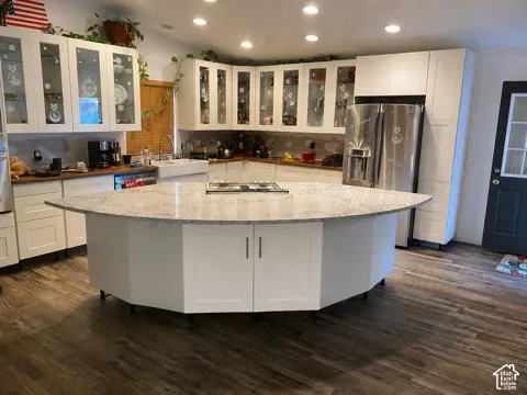 Spacious kitchen featuring an expansive center island with cooktop, white cabinetry with glass-front upper doors, wood-finish flooring, and recessed ceiling lighting