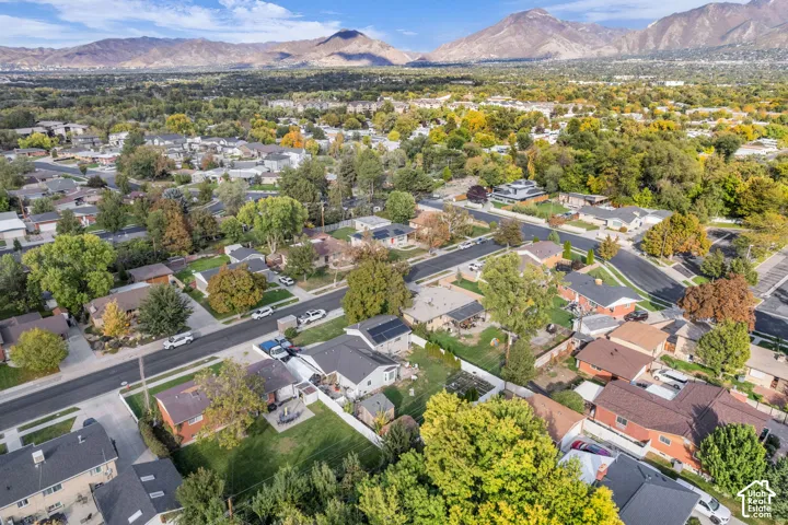 Aerial view showcasing a residential neighborhood nestled against mountain backdrop, featuring tree-lined streets, established landscaping throughout the community, and low-density single-family home construction with varied rooflines and architectural st