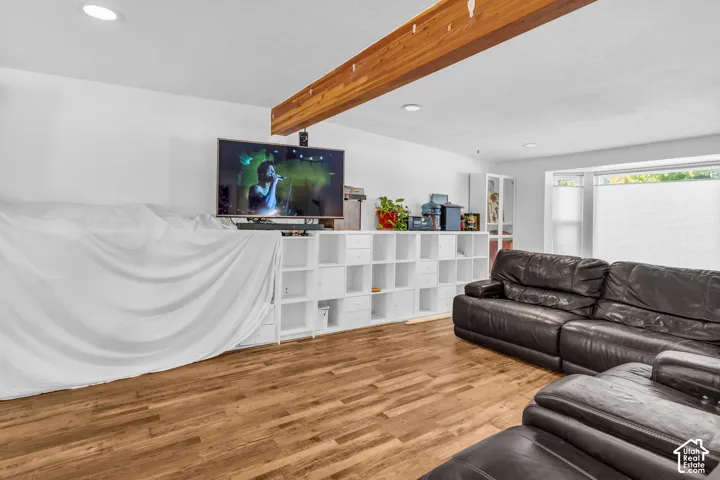 Wood-finish flooring with exposed ceiling beam, recessed lighting, built-in shelving, and a large window