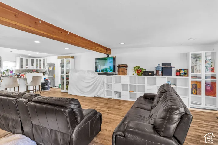 Open-concept living area with wood-finish flooring, exposed wood beam, recessed lighting, and white cabinetry