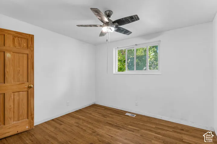 Hardwood flooring, natural wood panel door, white walls, ceiling fan with integrated lighting, and a multi-pane window